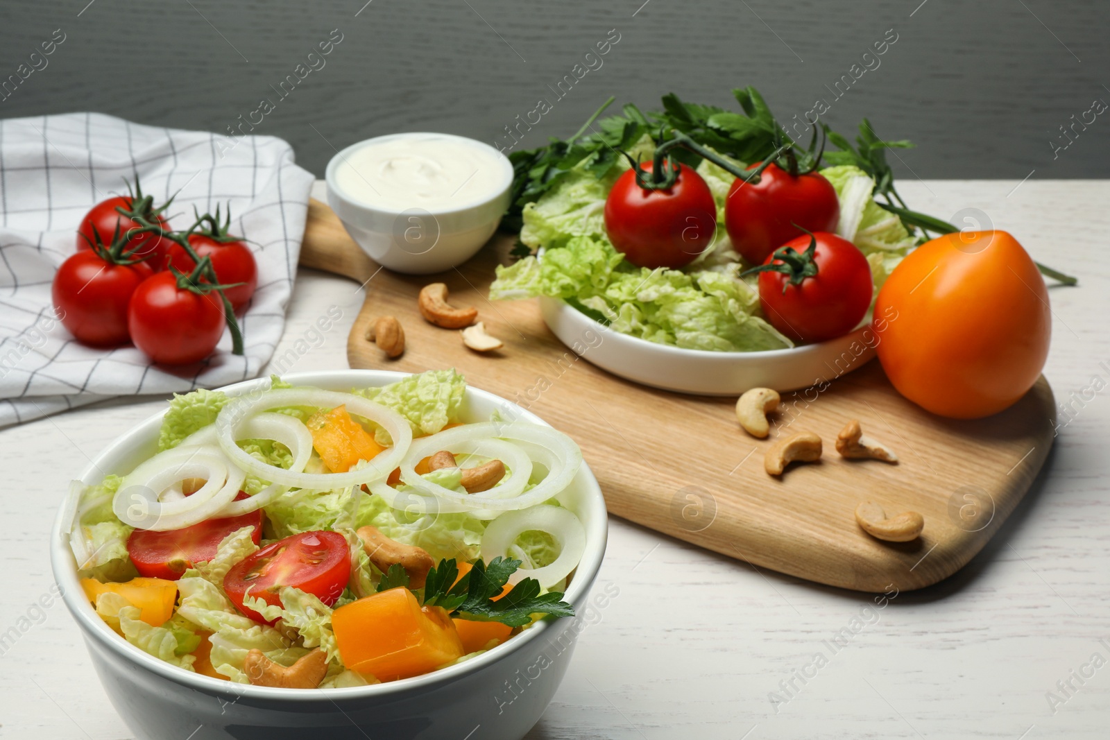 Photo of Bowl of delicious salad with Chinese cabbage, tomatoes and onion on white wooden table