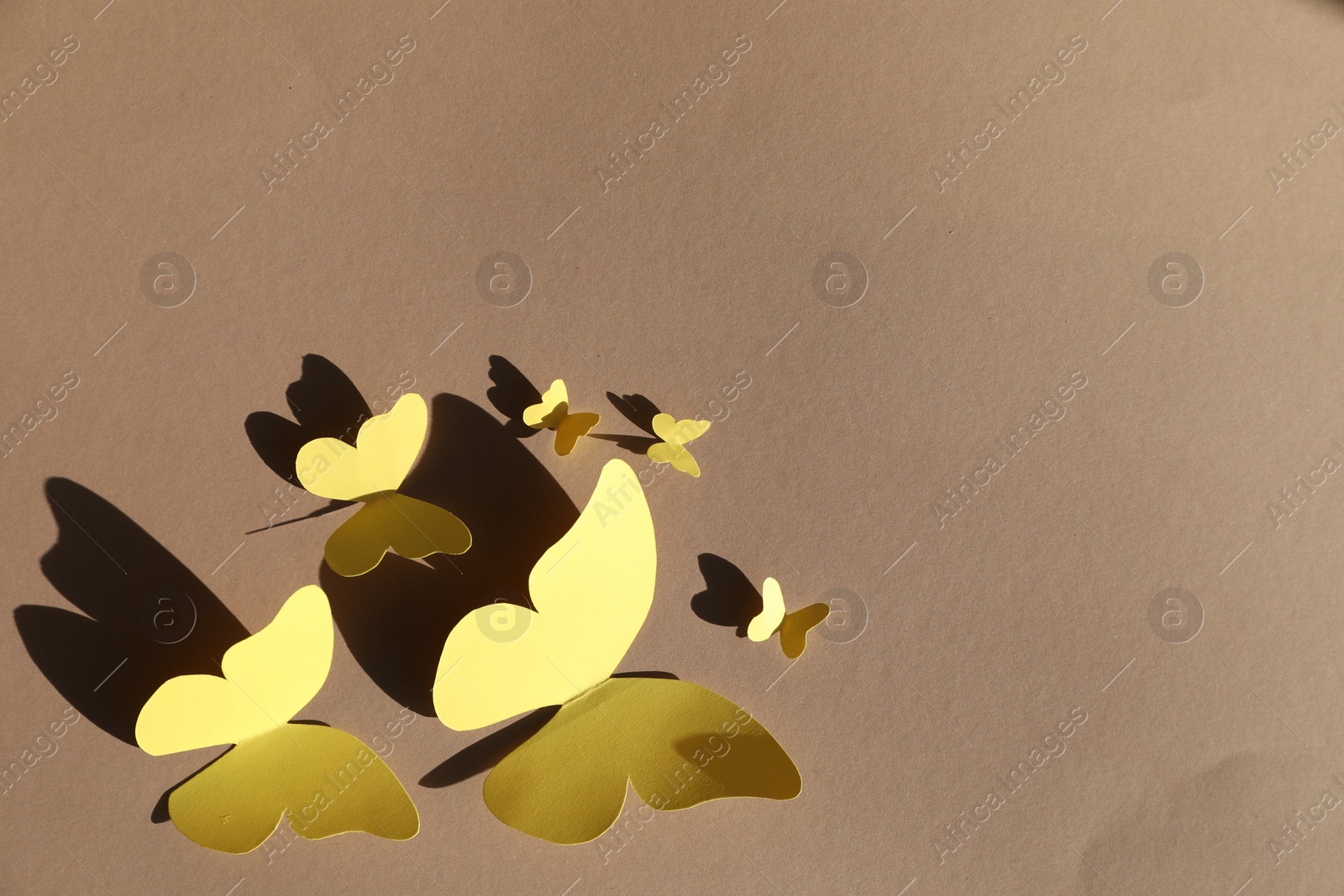 Photo of Yellow paper butterflies on light brown background, top view. Space for text