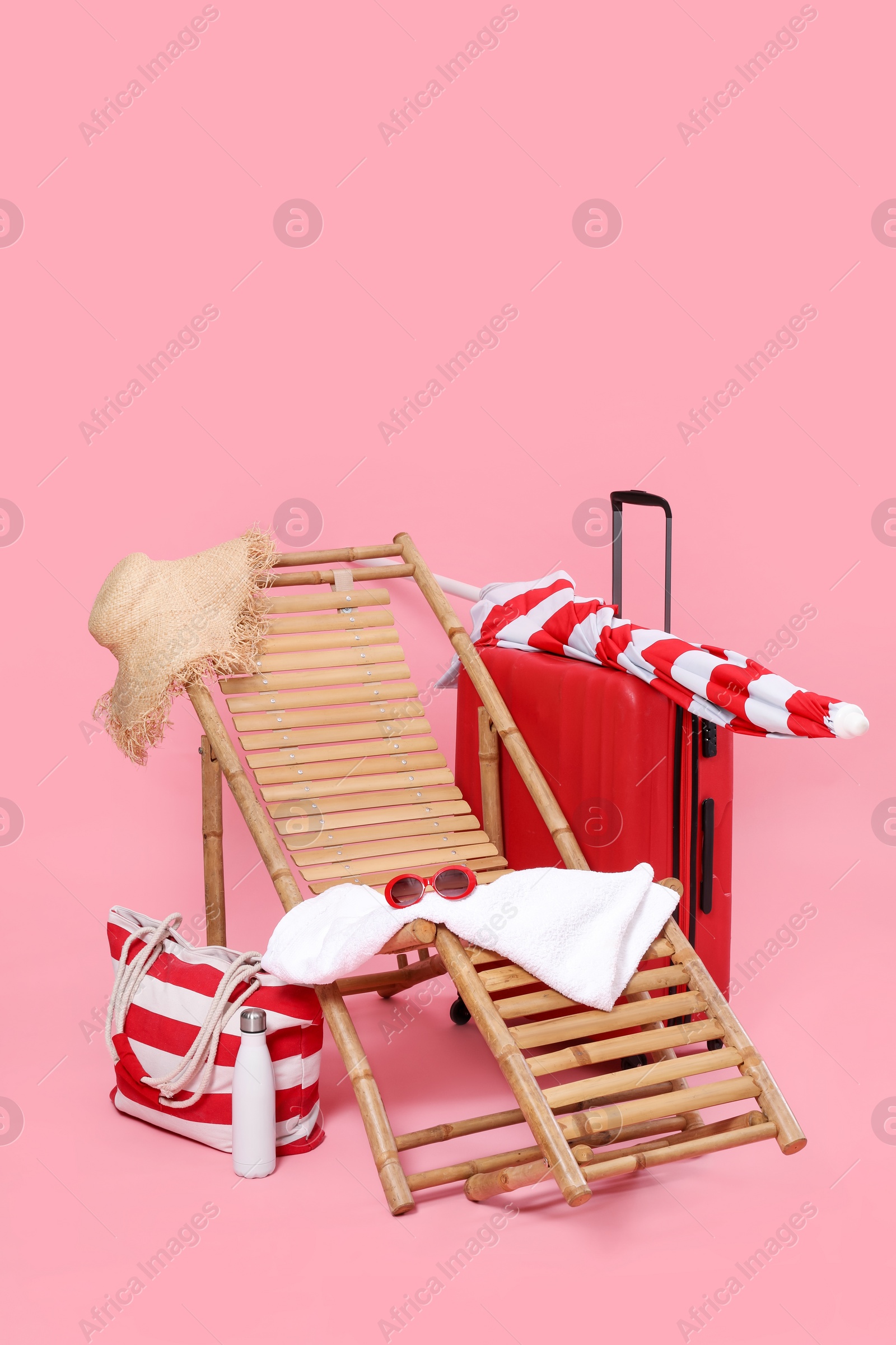 Photo of Deck chair, suitcase and beach accessories on pink background