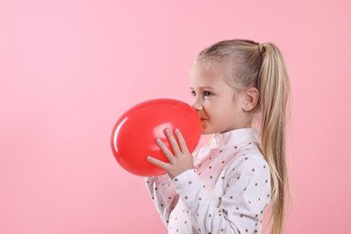Cute little girl inflating red balloon on pink background, space for text