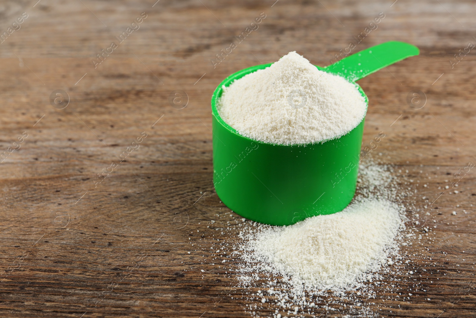 Photo of Measuring scoop of protein powder on wooden table. Space for text