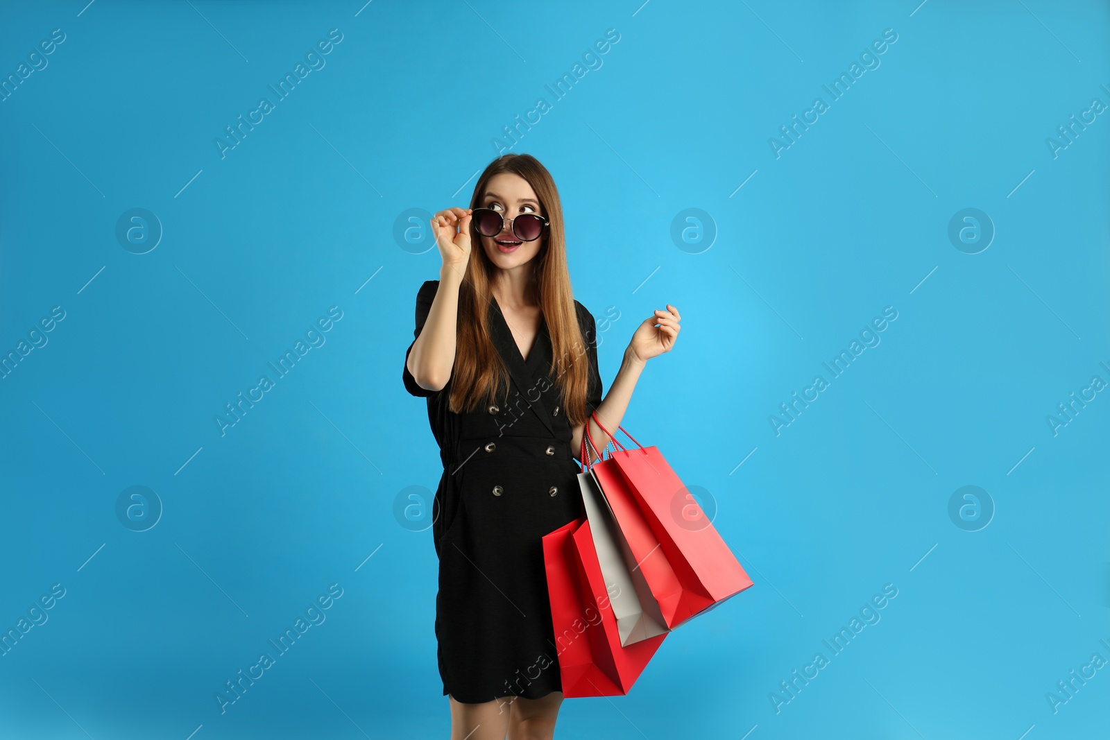 Photo of Beautiful young woman with paper shopping bags on light blue background