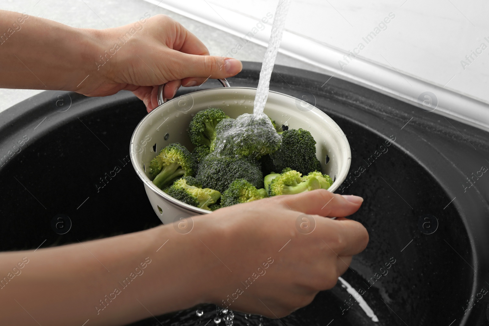 Photo of Woman washing fresh green broccoli in metal colander under tap water, closeup