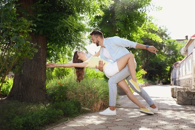 Lovely young couple dancing together in park on sunny day