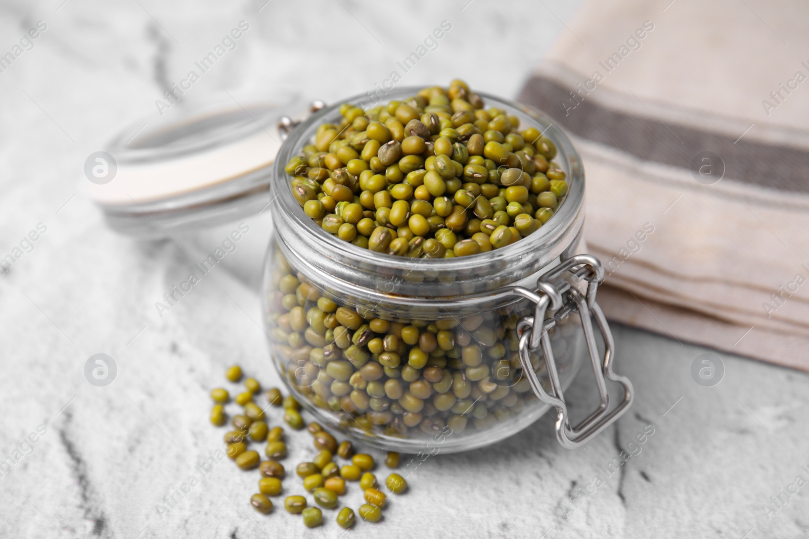 Photo of Glass jar with green mung beans on white textured table, closeup