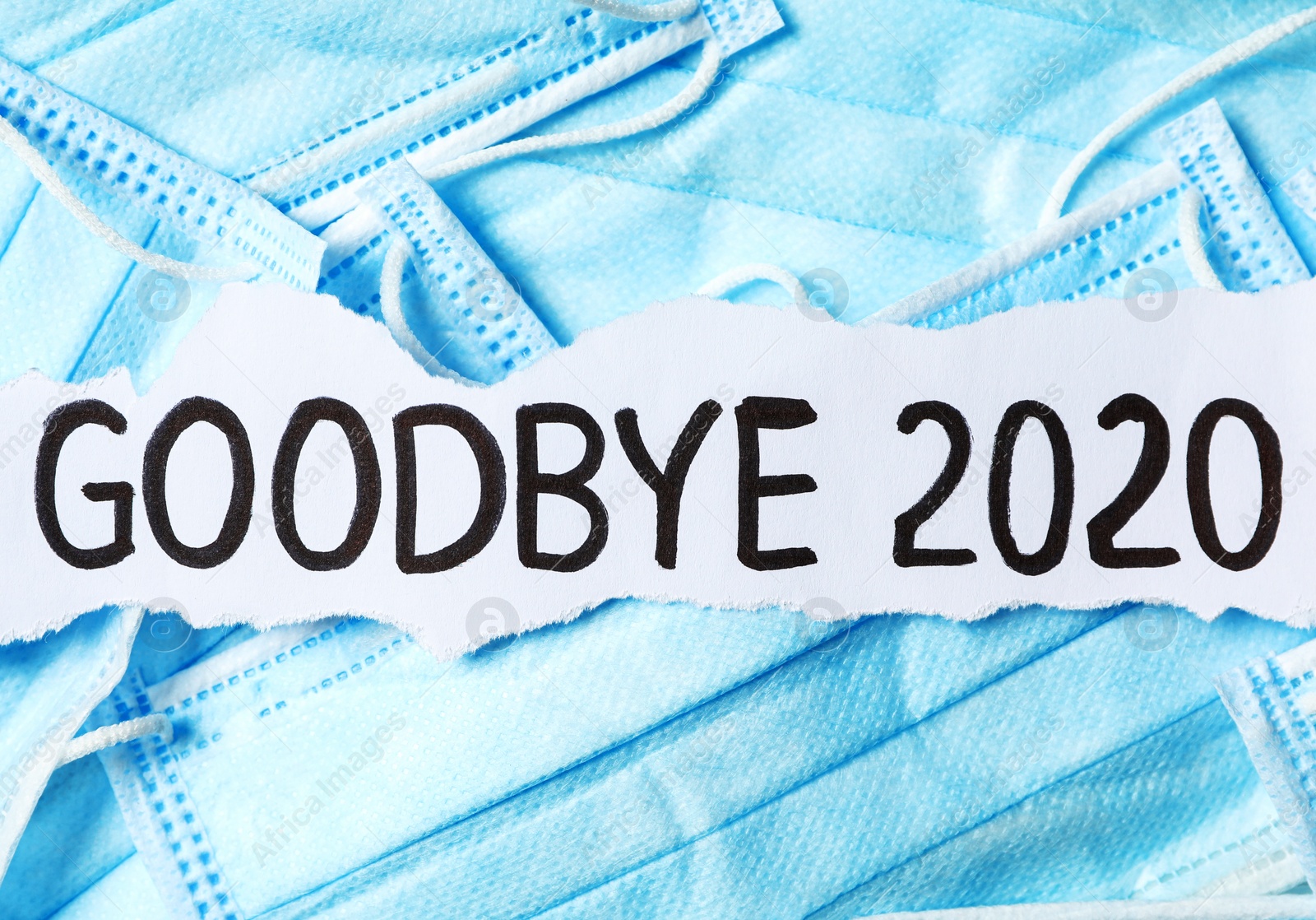 Photo of Piece of paper with phrase Goodbye 2020 on pile of blue medical masks. Coronavirus pandemic concept