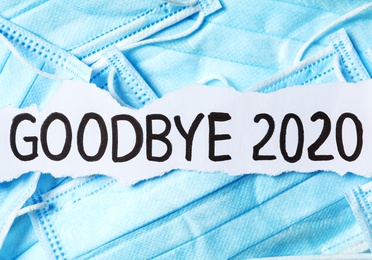 Piece of paper with phrase Goodbye 2020 on pile of blue medical masks. Coronavirus pandemic concept