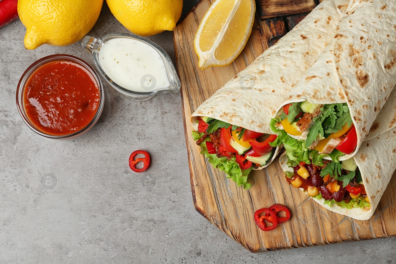 Photo of Board with delicious meat tortilla wraps on grey table, flat lay