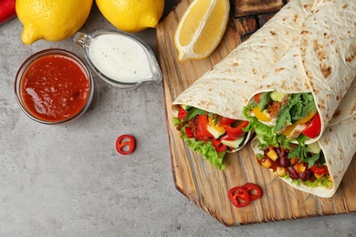 Board with delicious meat tortilla wraps on grey table, flat lay