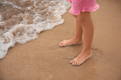 Little girl standing on sandy beach near sea, closeup. Space for text