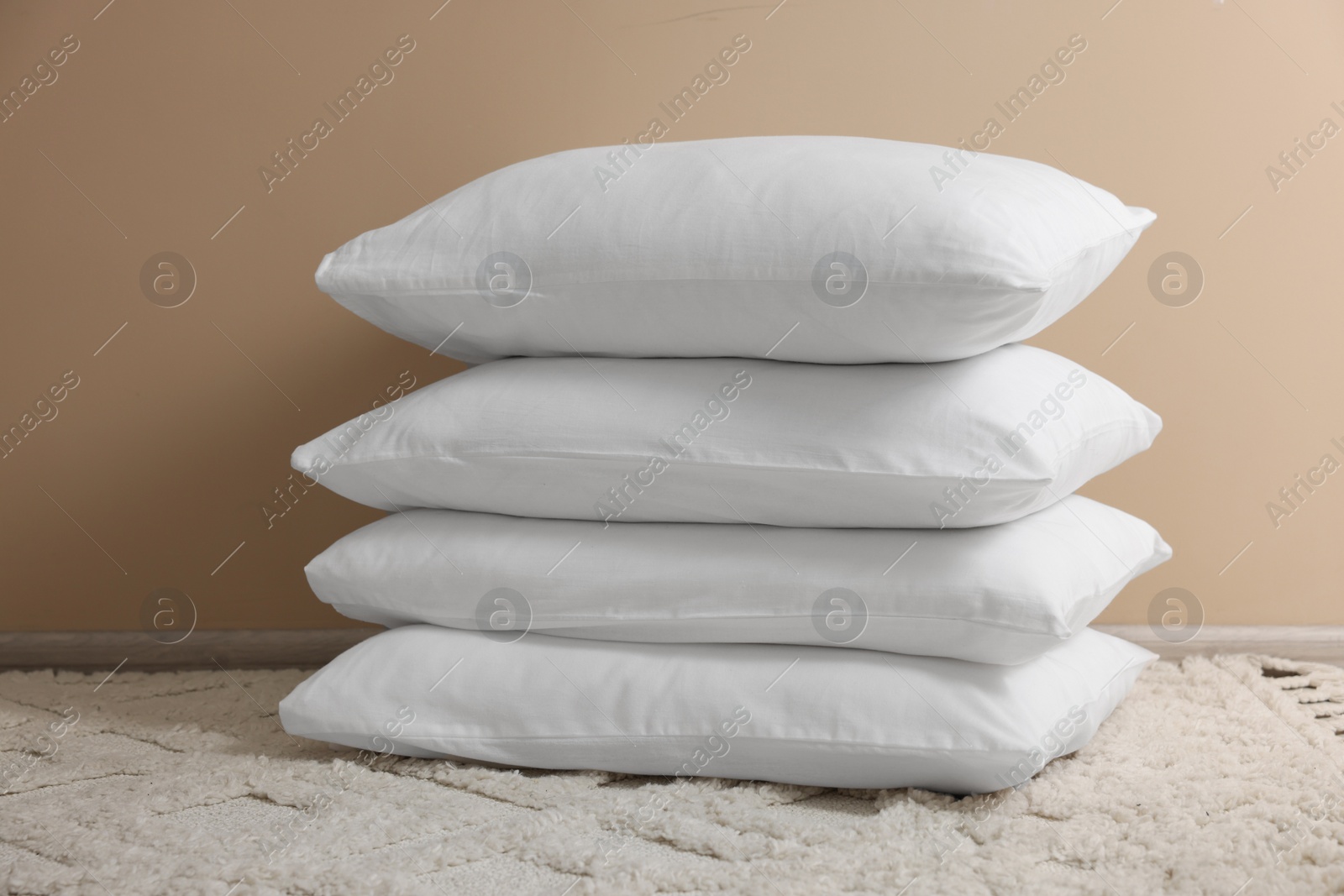 Photo of Stack of soft white pillows near beige wall indoors