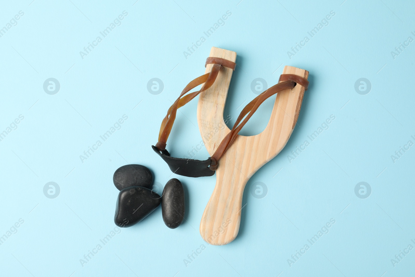 Photo of Wooden slingshot with stones on light blue background, flat lay