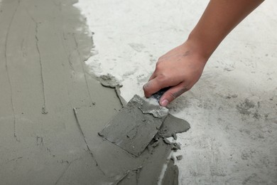 Photo of Worker with spatula applying adhesive mix for tiles on floor, closeup