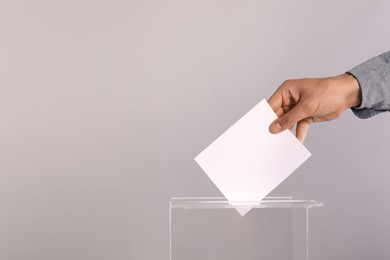 Photo of Man putting his vote into ballot box on light grey background, closeup. Space for text
