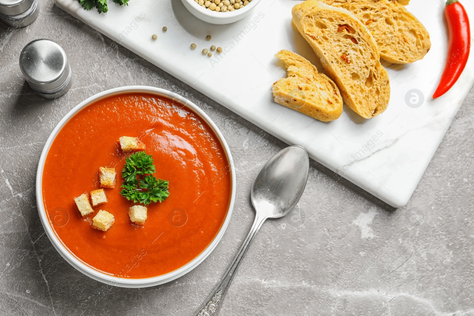 Photo of Fresh homemade tomato soup served with bread on grey table, top view. Space for text