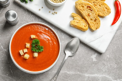 Fresh homemade tomato soup served with bread on grey table, top view. Space for text