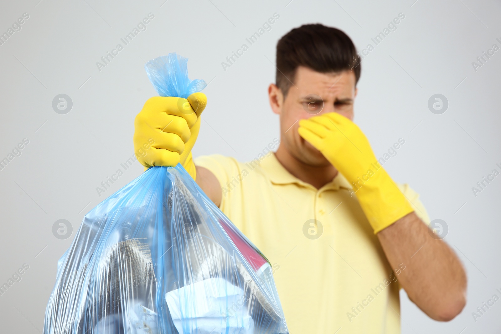 Photo of Man holding full garbage bag against light background, focus on hand