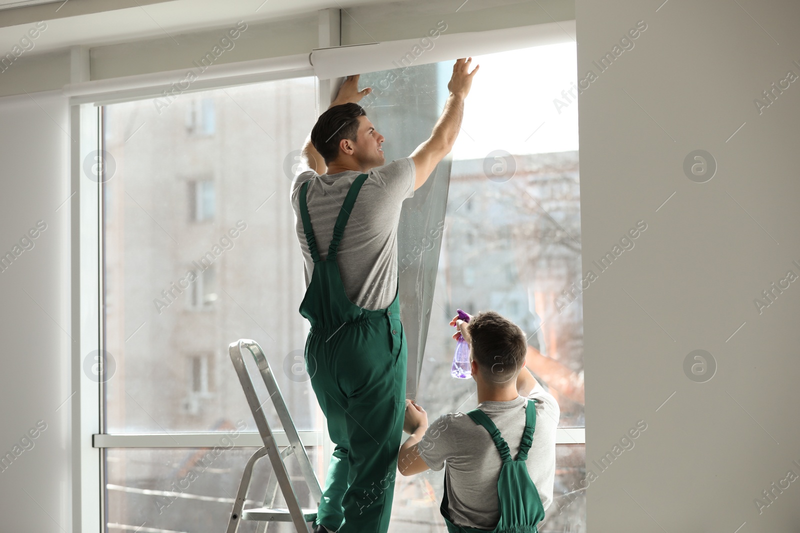 Photo of Professional workers tinting window with foil indoors