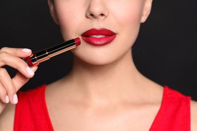 Photo of Young woman with beautiful makeup holding red lipstick on black background, closeup