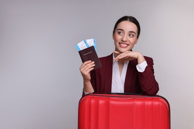 Happy businesswoman with passport, tickets and suitcase on grey background. Space for text