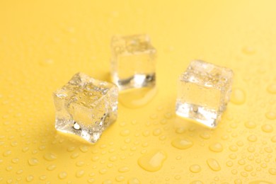 Photo of Crystal clear ice cubes on yellow background, closeup