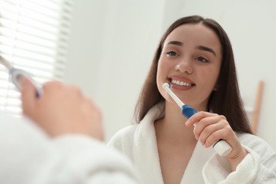 Young woman brushing her teeth with electric toothbrush near mirror in bathroom