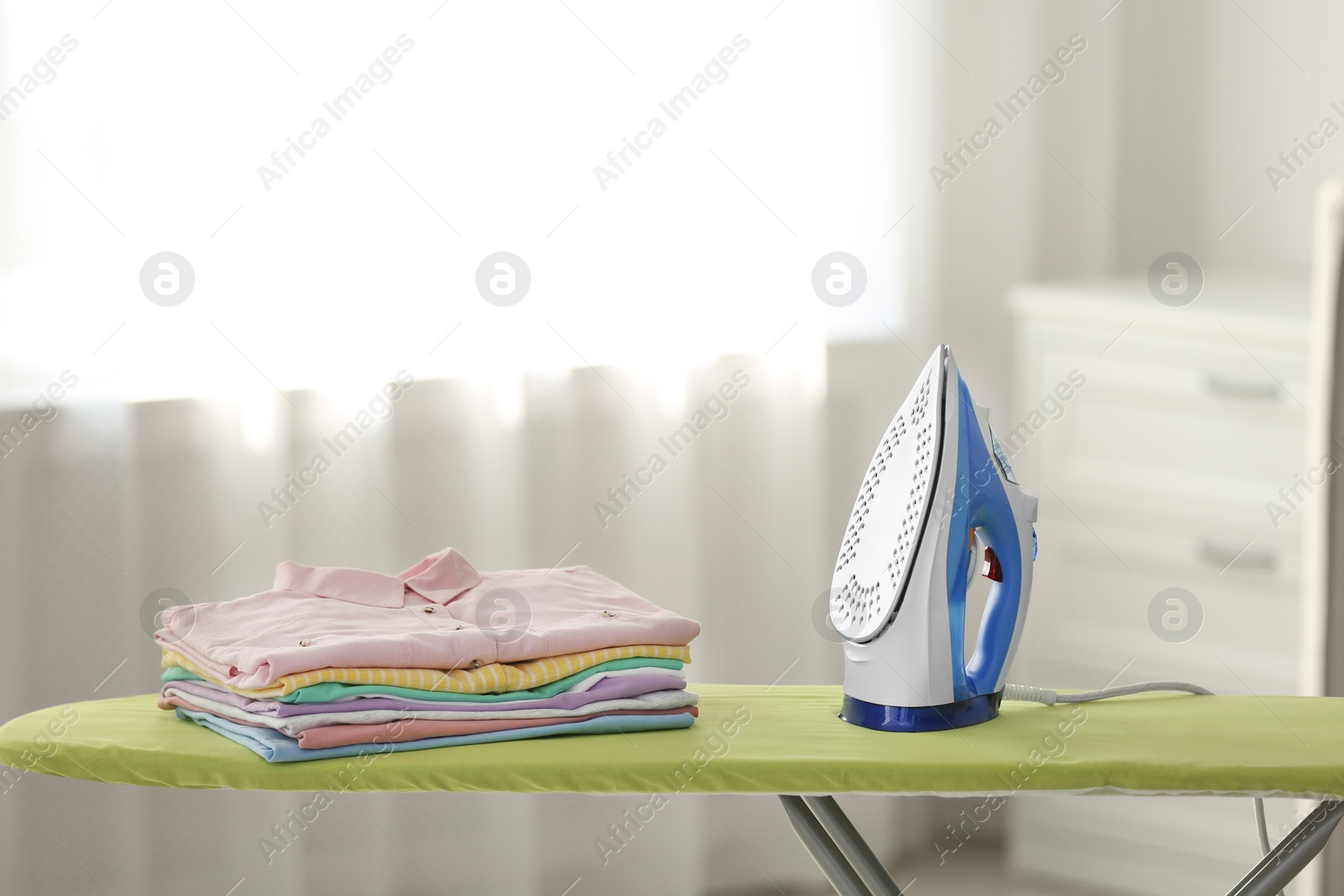 Photo of Board with modern iron and clean laundry at home