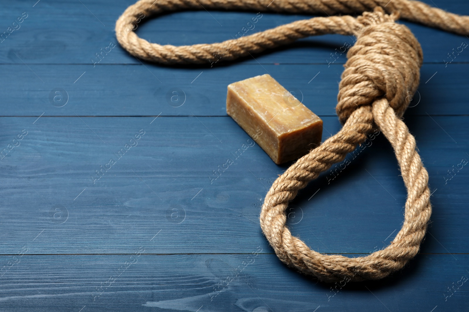 Photo of Rope noose and soap bar on blue wooden table. Space for text