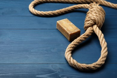 Rope noose and soap bar on blue wooden table. Space for text