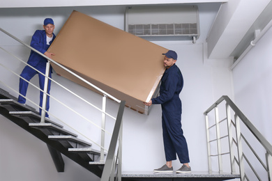 Professional workers carrying refrigerator on stairs indoors