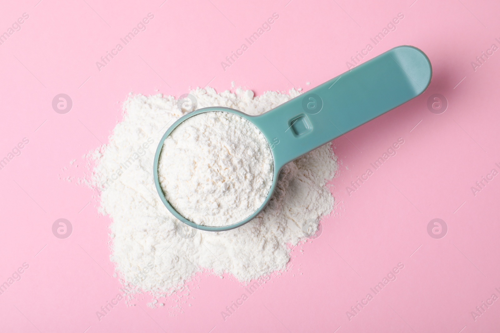 Photo of Scoop and pile of protein powder on pink background, flat lay