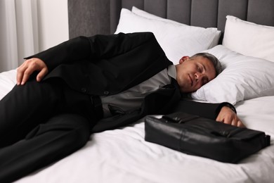 Photo of Businessman with briefcase sleeping on bed indoors