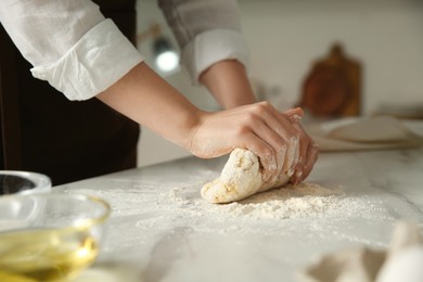 Photo of Woman kneading dough at table in kitchen, closeup