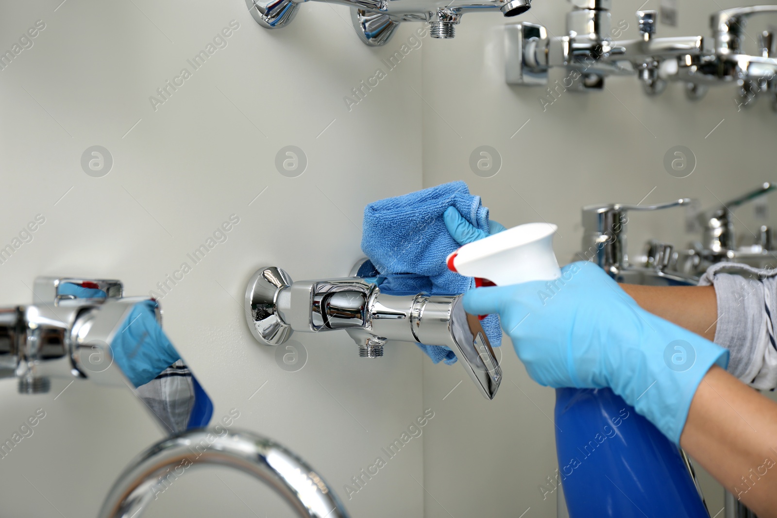 Photo of Woman cleaning faucets with rag and detergent in bathroom fixtures store, closeup