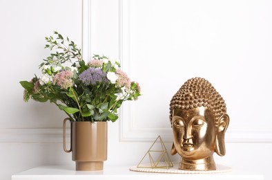 Photo of Stylish ceramic vase with beautiful flowers and golden Buddha sculpture on table near white wall