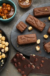 Delicious chocolate candy bars with caramel and nuts on grey table, flat lay