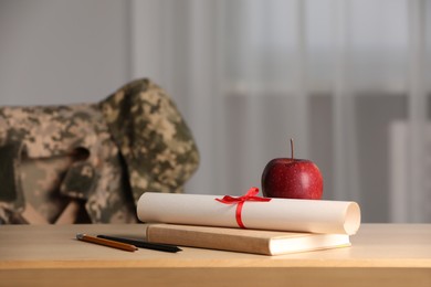 Diploma, apple and stationery on wooden table indoors. Military education
