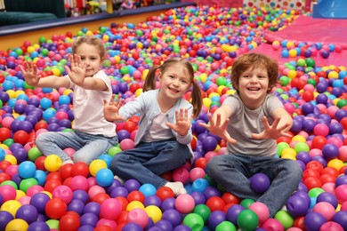 Photo of Happy little kids sitting on colorful balls in ball pit