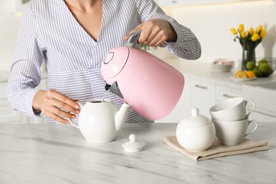 Photo of Woman pouring hot water from modern electric kettle in cup indoors, closeup