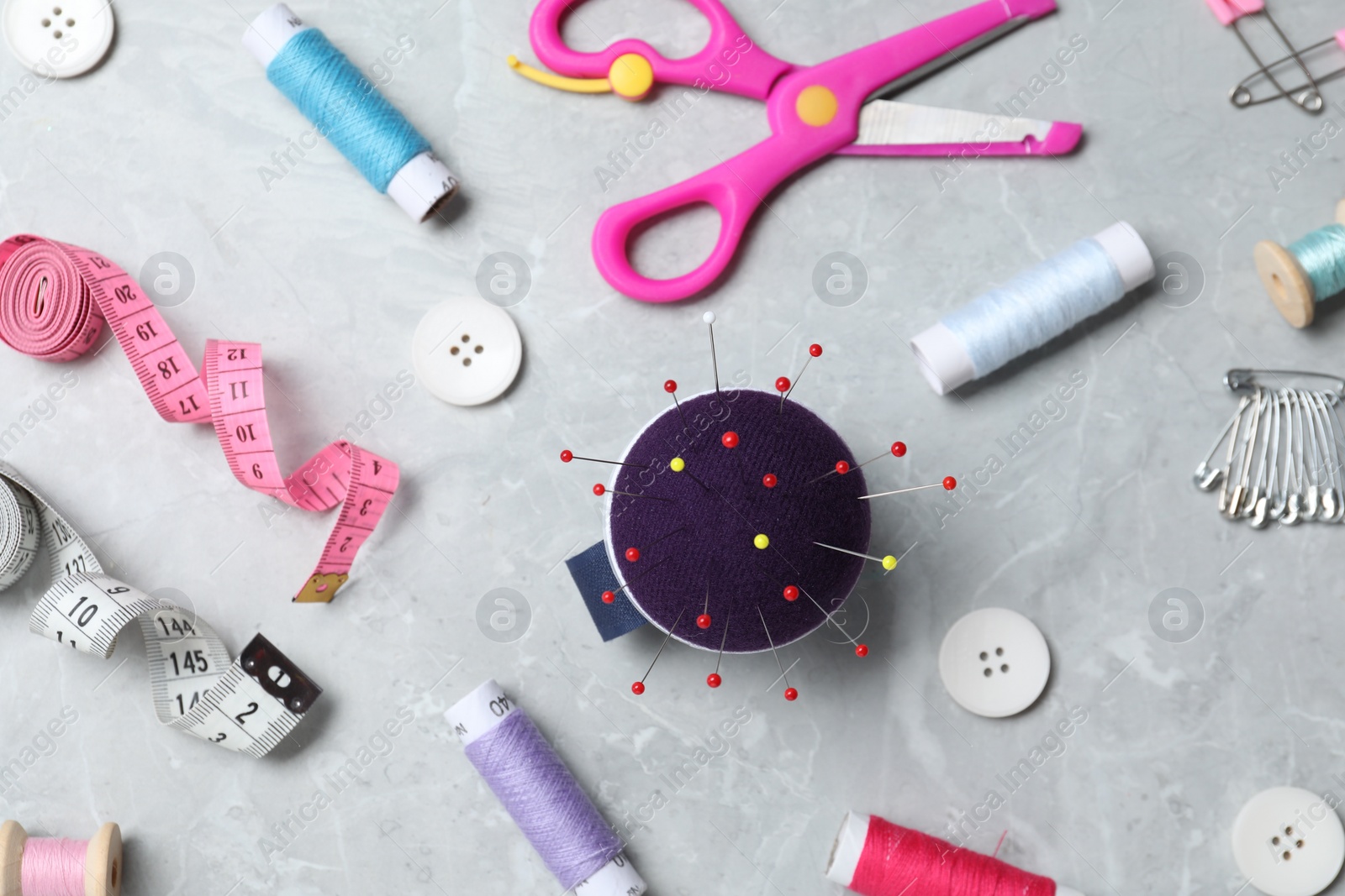 Photo of Blue pincushion with pins and other sewing tools on grey table, flat lay