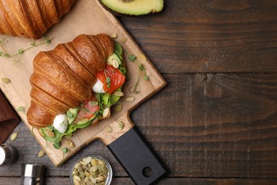 Photo of Tasty croissant with salmon, avocado, mozzarella and lettuce served on wooden table, flat lay. Space for text