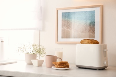 Photo of Modern toaster, flowers and tasty breakfast on counter in kitchen