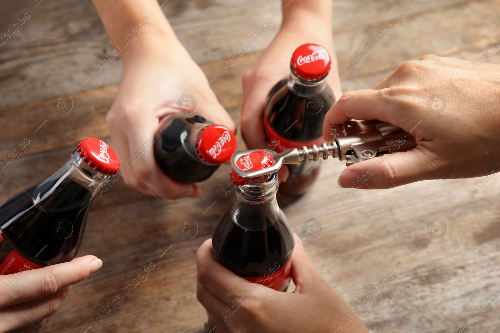 Photo of MYKOLAIV, UKRAINE - NOVEMBER 15, 2018: People with bottles of Coca Cola at wooden table, closeup