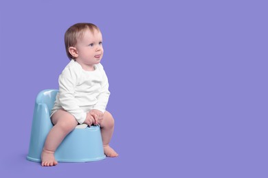 Photo of Little child sitting on baby potty against violet background, space for text