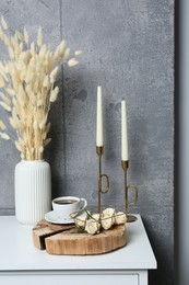 Photo of Cup of coffee, vase and other decor on white table near grey wall indoors. Interior design