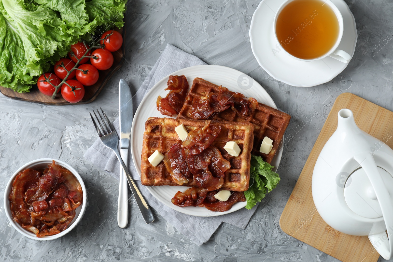 Photo of Delicious Belgium waffles served with fried bacon and butter on grey table, flat lay