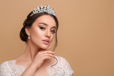 Beautiful young woman wearing luxurious tiara on beige background, space for text