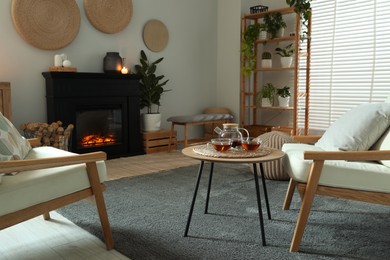 Photo of Stylish fireplace near coffee table with tea in cosy living room. Interior design