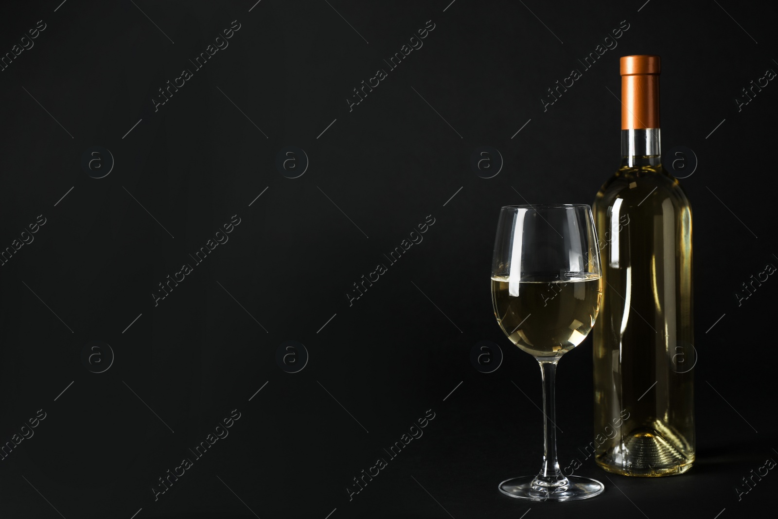 Photo of Bottle and glass of expensive white wine on dark background