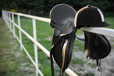 Leather horse saddle and helmet on wooden fence outdoors